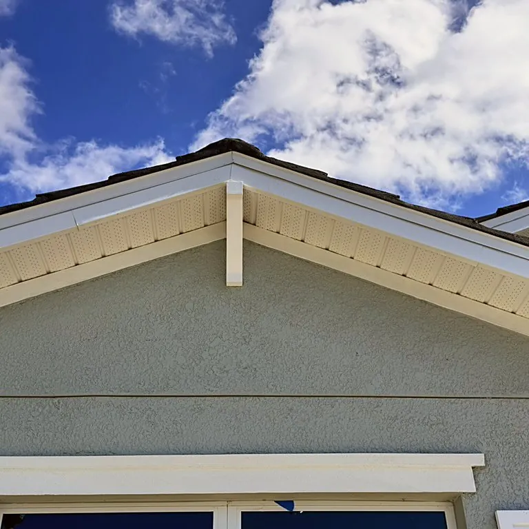 White vented soffit and fascia under a gable roof edge, with a bracket against a blue stucco wall